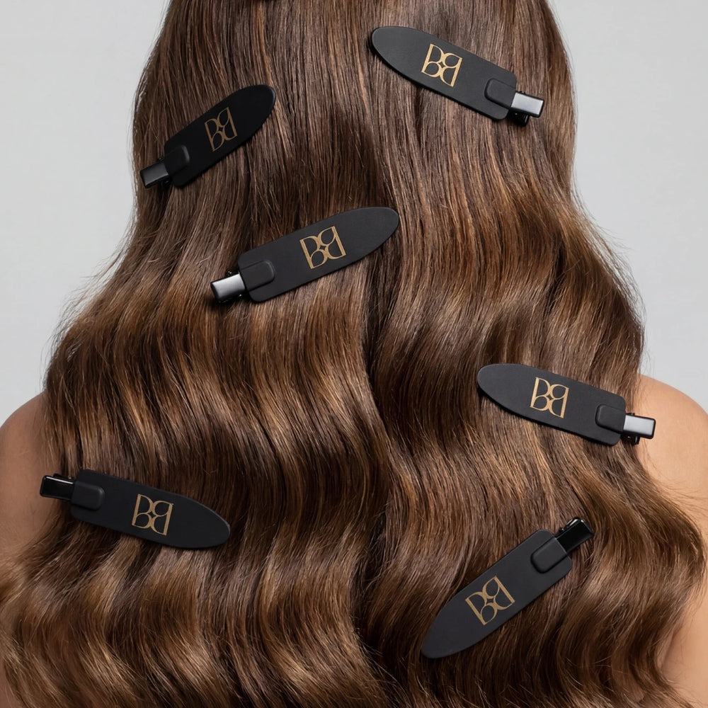 Black hair clips with BB logo on a person's hair against a neutral background