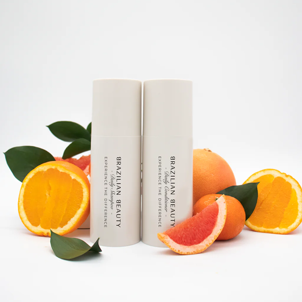 Brazilian Beauty Daily Shampoo and Daily Conditioner surrounded by oranges and grapefruits on a neutral background.