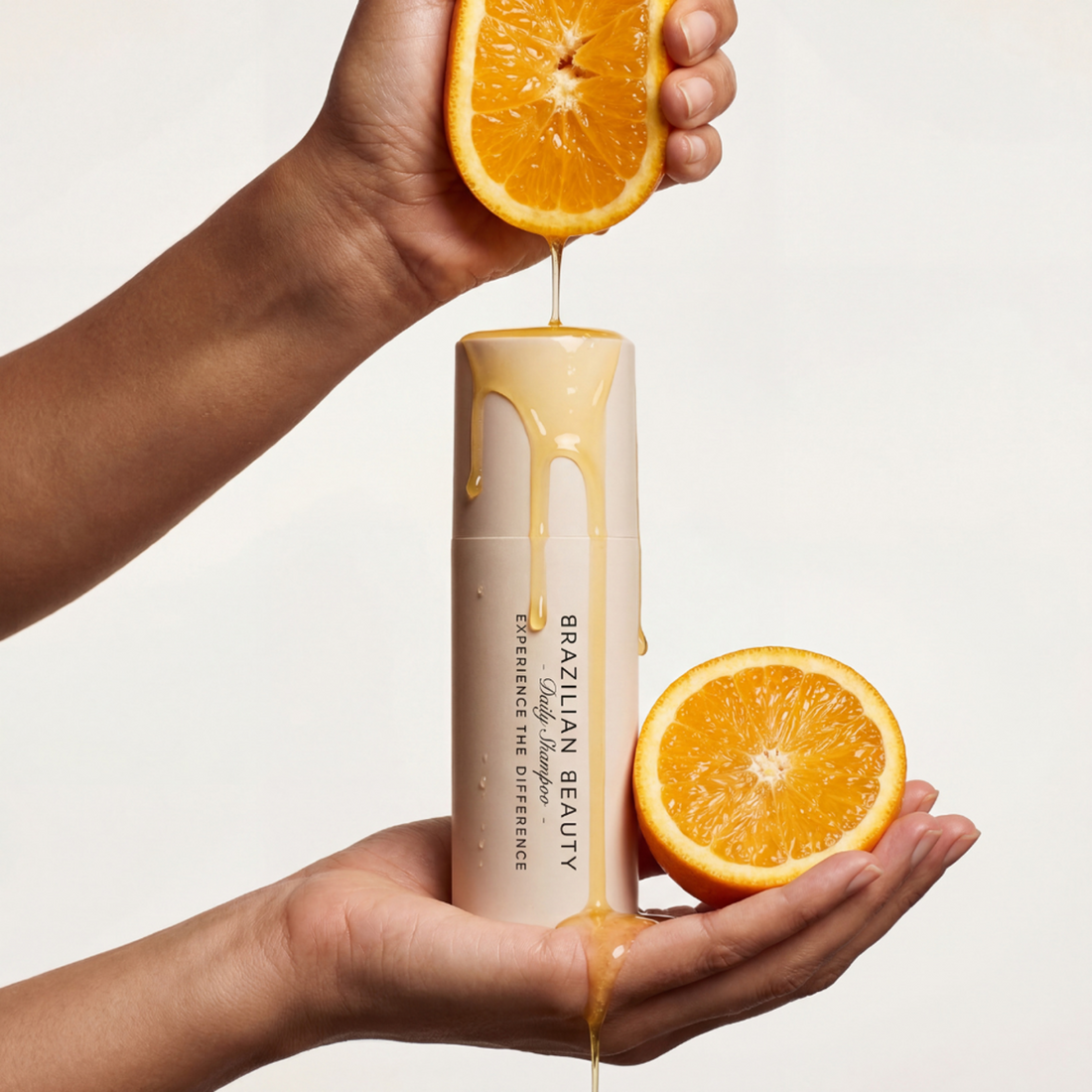 Hand holding an orange and squeezing orange juice on to a bottle of Brazilian Beauty Daily Shampoo. 